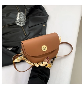 Detail of a brown saddle bag featuring a gold chain handle wrapped in a silk scarf