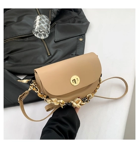 Detail of beige saddle bag featuring gold clasp and silk scarf wrapped chain handle