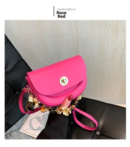 Detail of rose red saddle bag with gold circular lock and silk ribbon chain strap