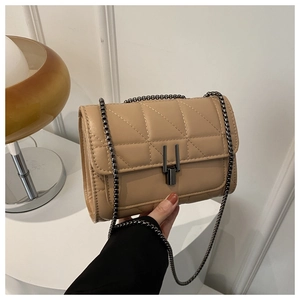 Detail of quilted beige crossbody bag featuring gunmetal chain and unique metal buckle