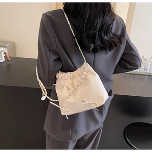 Detail of cream white pleated bucket bag with bow accents and metal chain strap