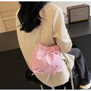 Detail of pink pleated crossbody bag with chain strap and decorative bows worn by model