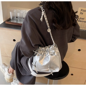 Silver metallic bucket bag with decorative bows and chain strap worn by a model
