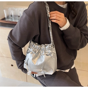 Silver drawstring bucket bag with metallic finish and bow details on a chain strap