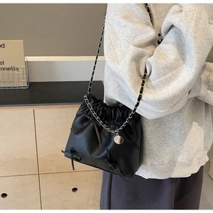 Détail d'un sac seau noir en cuir à cordon avec nœuds décoratifs et bandoulière en chaîne