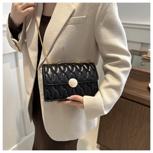 Détail d'un sac à bandoulière matelassé noir porté avec une veste élégante en tweed blanc