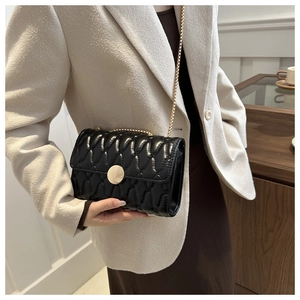 Détail d'un sac matelassé noir à chaîne dorée porté sur un manteau blanc élégant