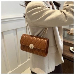 Détail d'un sac bandoulière matelassé marron avec boucle dorée et chaîne élégante