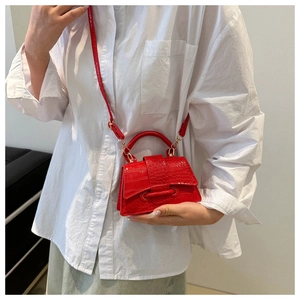 Detail of red mini crossbody bag with crocodile texture and gold hardware on model