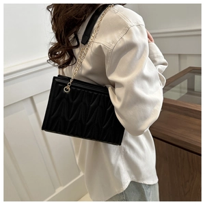 Detail of wave quilted pattern on black square chain bag with golden hardware strap
