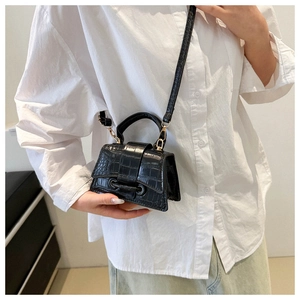 Detail of black faux crocodile leather mini bag with gold hardware on white shirt