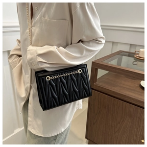 Detail of black quilted shoulder bag featuring V-shaped texture and golden chain strap