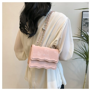 Sac bandoulière rose à rabat ondulé et chaîne porté par un mannequin dans un décor