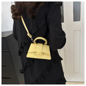 Close-up of bright yellow croc-embossed mini bag styled with a black pleated dress