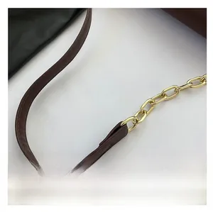 Detail of the brown leather shoulder strap combined with a gold metal chain links