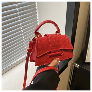 Close-up of red crocodile embossed handbag with golden buckle and adjustable strap