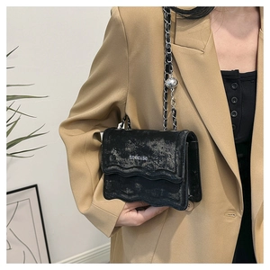Detail of black square chain bag with wavy edge and vintage silver coating on a model