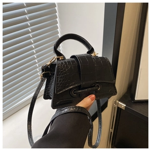 Detail of black glossy crocodile pattern crossbody bag with round handle and top flap