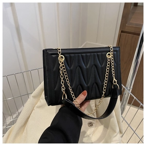 Close-up of black crossbody bag with wave quilting and gold chain in a basket