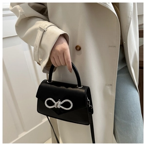 Detail van zwarte crossbodytas met kristallen strik en mat lederen afwerking