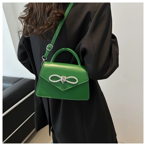 Detail van een felgroene crossbodytas met een fonkelende zilveren strik van strassteentjes