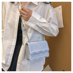 Detail of light blue suede crossbody bag with wave edge flap and silver chain ball