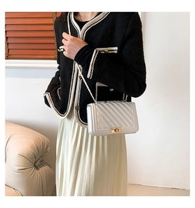 Detailed view of a white quilted crossbody bag with gold lock and chain strap on a model