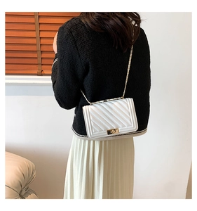 Detailed view of white quilted chain bag with gold metal twist lock on a model