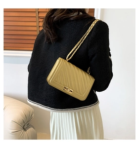 Detail of a yellow V-stitch shoulder bag with a metal chain strap shown on a model