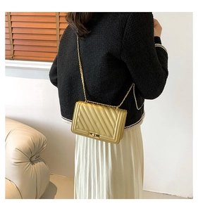Detail of a gold crossbody bag with chevron quilting and golden metal chain strap