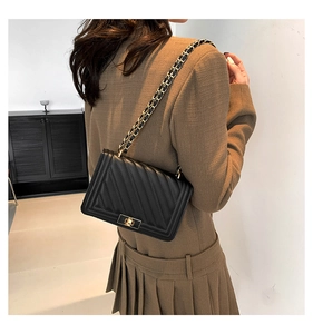 Detail of black quilted shoulder bag with gold chain strap and square metal clasp lock