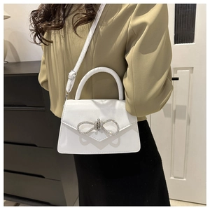 Detailweergave van een witte crossbodytas met een grote glinsterende strass-strik decoratie
