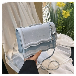 Détail du sac à chaîne bleu clair avec rabat ondulé et pendentif sphérique en métal