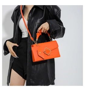 Detail of orange crocodile pattern handbag with gold buckles and pleated handle wrap