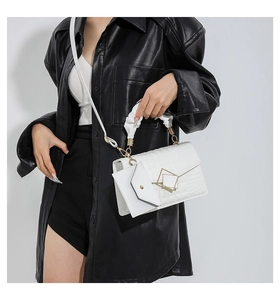Close-up of white quilted handbag featuring a geometric metal lock and pleated handle