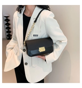 Detail of minimalist black crossbody bag with gold buckle and chain strap on model