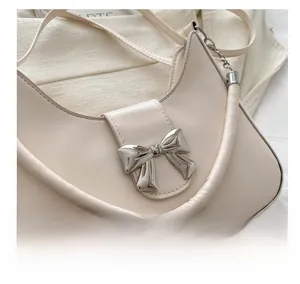 Dettaglio della borsa a mezzaluna avorio con fiocco in metallo argento e texture in ecopelle