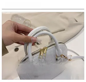 Detail view of a white crocodile pattern shell bag with golden zippers and dual handles