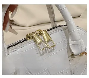Detail shot of smooth golden metal zippers on a white crocodile texture shell bag