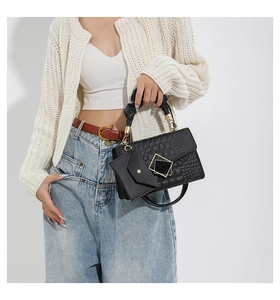Detail view of black pleated handbag with quilted texture and mini pouch accessory