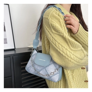 Detail view of the blue textured crossbody bag with silver chain and brand logo