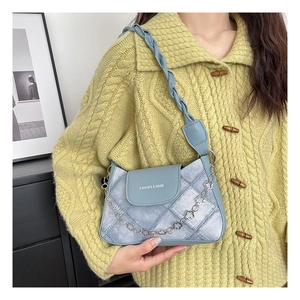 Close-up of light blue textured shoulder bag with floral silver chain and woven strap