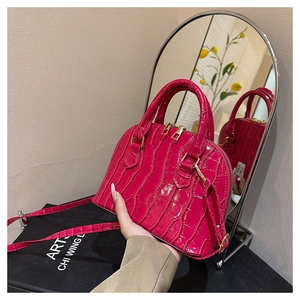 Detail of rose red shell bag with crocodile texture, gold hardware and leather strap