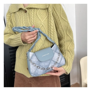 Detail of light blue faux leather underarm bag with quilted texture and metal chain strap