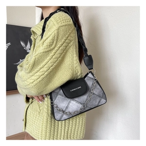 Quilted gray underarm bag with black leather flap and silver chain on green sweater