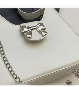 Close-up of white leather handbag with silver bow buckle and delicate metal chain strap