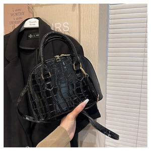Detail of black faux leather shell bag featuring crocodile texture and gold hardware