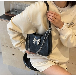 Detail of black leather underarm bag featuring a silver bow buckle and decorative chain