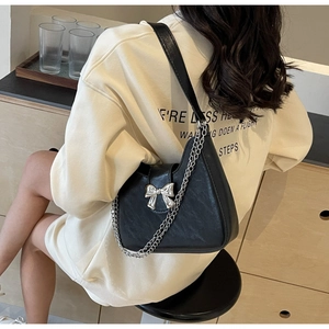 Detail of minimalist black leather shoulder bag featuring a silver metal bow and chain strap