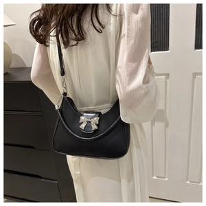 Dettaglio borsa a sella hobo nera con fiocco argento e catena su un abito bianco